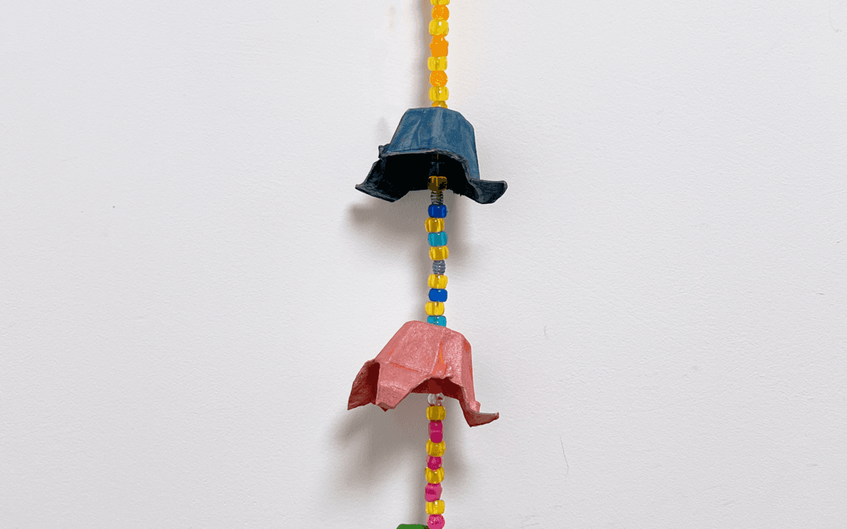 Photographie d'une suspension murale faite à partir de boîtes d'œufs peintes et de perles, le tout de différentes couleurs : rose, jaune, bleu, vert et orange.